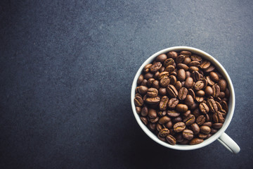 White coffee cup filled with coffee seeds on black surface background.