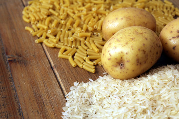 Rice, potatoes and macaroni pasta on a wooden table.Three common carbohydrates which provide energy but can cause obesity