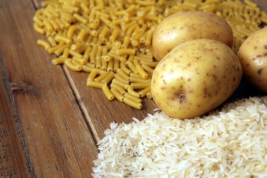 Rice, potatoes and macaroni pasta on a wooden table.Three common carbohydrates which provide energy but can cause obesity