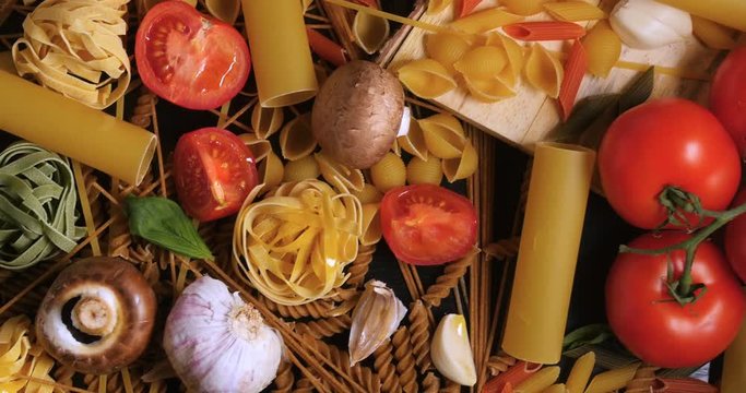 Dolly tilt down view of different variety of Italian pasta and ingredients