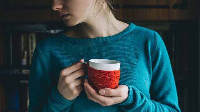 Young woman in mint-colored sweater drinking hot coffee from Mug in red knitted mitten. Bundled up, get warm concept