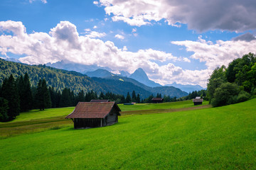 Fototapeta na wymiar Beautiful view of idyllic mountain scenery in the Alps with traditional chalet and fresh green pastures blooming flowers on a sunny day blue sky clouds in summer