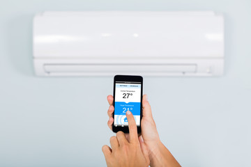 Woman Operating Air Conditioner Using Smartphone