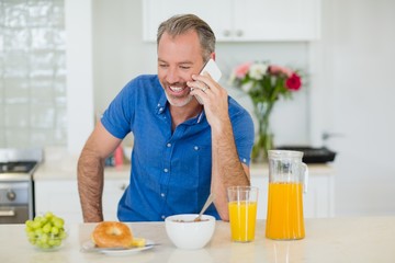 Fototapeta na wymiar Man talking on mobile phone while having breakfast in kitchen
