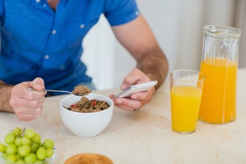 Man using mobile phone while having breakfast in kitchen