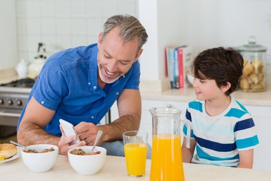 Father showing mobile phone to son while having breakfast
