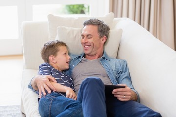 Obraz premium Father and son lying on sofa with digital tablet in living room