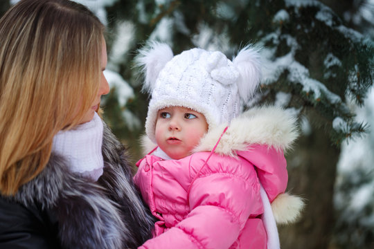 Mother holds daughter on hands and talking to her in the open air. Family walk in a winter park. Family happiness.