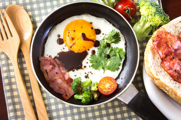 Breakfast with fried egg and bacon in dark pan on the table