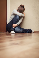 Frau sitzt verängstigt in einer Ecke, häusliche Gewalt