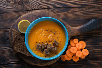 Blue bowl with carrot soup, rustic wooden setting, above view
