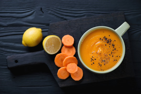 Bowl of carrot cream-soup over black wooden background, top view