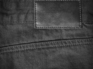 Black denim textile for background back closeup with leather label