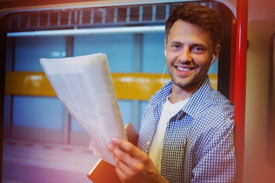 Portrait of handsome man holding newspaper while listening music