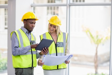 Architects holding blueprint discussing over digital tablet
