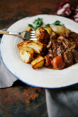 Beef bourguignon in ceramic plate with baked potatoes on metallic background. Rustic concept, natural light.
