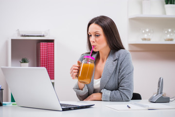 Young businesswoman is drinking smoothie in her office.