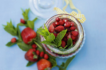 strawberry harvest. strawberries in a glass jar with a yellow ribbon and mint on blue cotton tablecloth  2