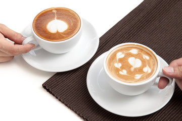 Two coffee cups of latte art heart shape place on napkin on whit