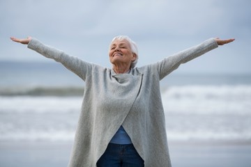 Senior woman with arms outstretched standing on the beach - Powered by Adobe