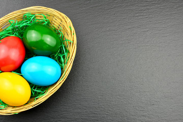 Oster Motiv - Bunte Ostereier in einem Strohkorb auf einer Schieferplatte mit Textfreiraum