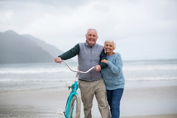 Senior couple standing with bicycle on the beach
