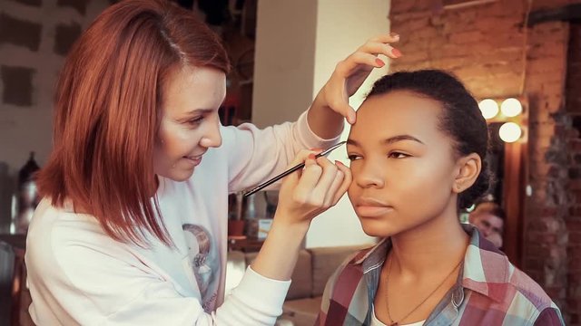 Makeup artist doing make-up beautiful african model.