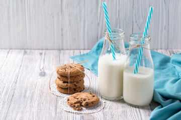 Bottles of milk and chocolate chip cookies on wooden background