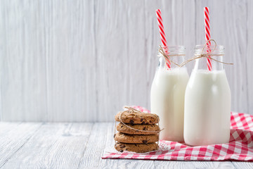 Bottles of milk with red striped straws and chocolate chip cookies on wooden background - Powered by Adobe