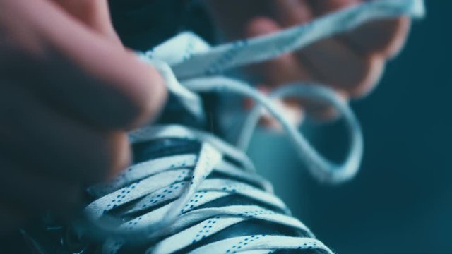 EXTREME CU Caucasian ice hockey player tightening laces on his skates in the locker room, preparing for the game. 4K UHD RAW edited footage
