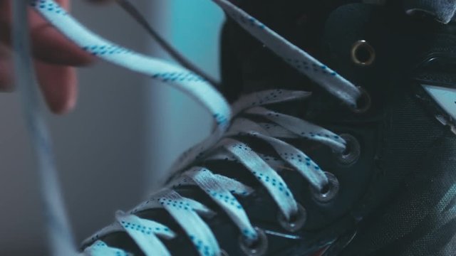 EXTREME CU Caucasian ice hockey player tightening laces on his skates in the locker room, preparing for the game. 4K UHD RAW edited footage