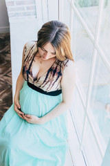 Pregnant woman in dress sitting by window 