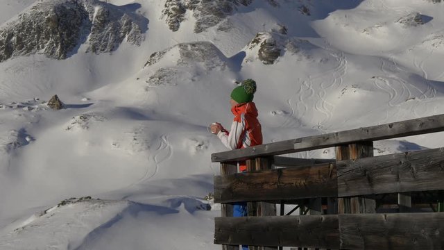 Woman drinking tea on the terrace in the mountains on the background of the ski slopes in the ski resort