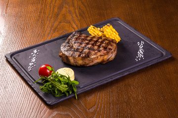 Grilled beef steak with corn and tomato on a black slate board