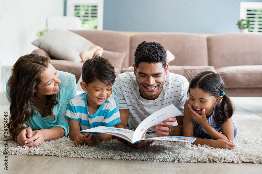 Wall mural Mixed race parents and children lying on rug reading book 