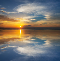 Sun in the clouds above the seascape with mirror reflection