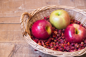 Rosehip and red apples lying in wicker basket on boards