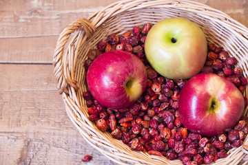 Basket with rosehip and red apples on wooden surface