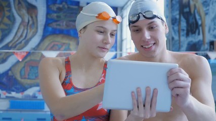 Athletes Swimmers Using a Digital Tablet. Male and female athletes swimmers using a digital tablet. Analyze the data on the swim. - Powered by Adobe
