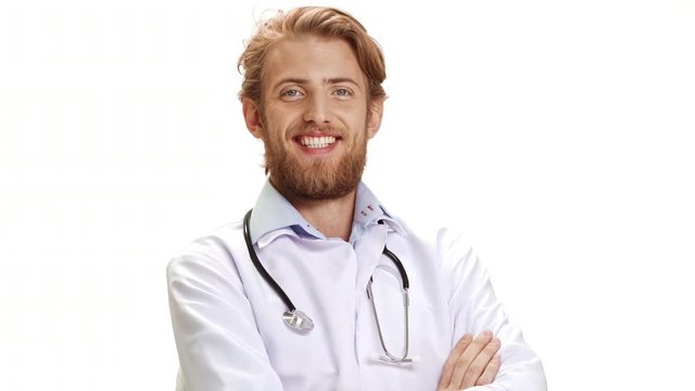 Smiling handsome Caucasian light bearded male doctor standing with arms folded on white background