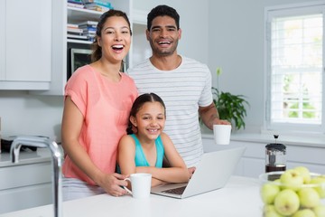 Family using laptop while having coffee in kitchen