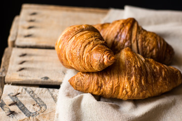 Heap of fresh croissants with golden crust on linen cloth, vintage wood box, rustic interior, copyspace, poster template, mockup for cafe or restaurant
