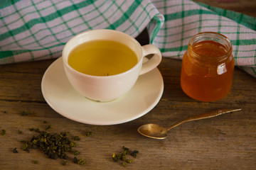 Green tea in a white cup and jar of honey with spoon and green k