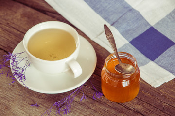 Green tea in a white cup and jar of honey with spoon and blue ki