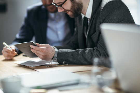 Two businessmen reading together from tablet and smiling.
