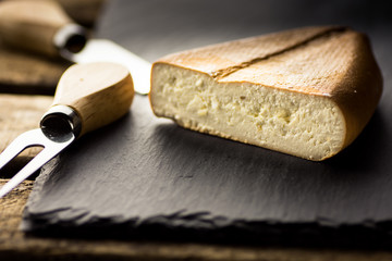 Chunk of smoked goat cheese with fork and knife in the background, black stone board, vintage wood box,rustic interior