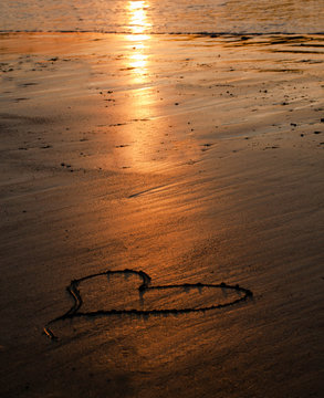 heart painted in the beach sand at sunset