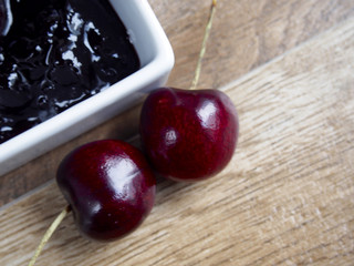 Cherry jam with two cherries on wood background