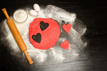 Red hearts Cutting dough with eggs, flour and rolling pin on a black table. top view