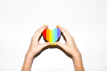 Painted heart shaped lgbt flag in hands on white